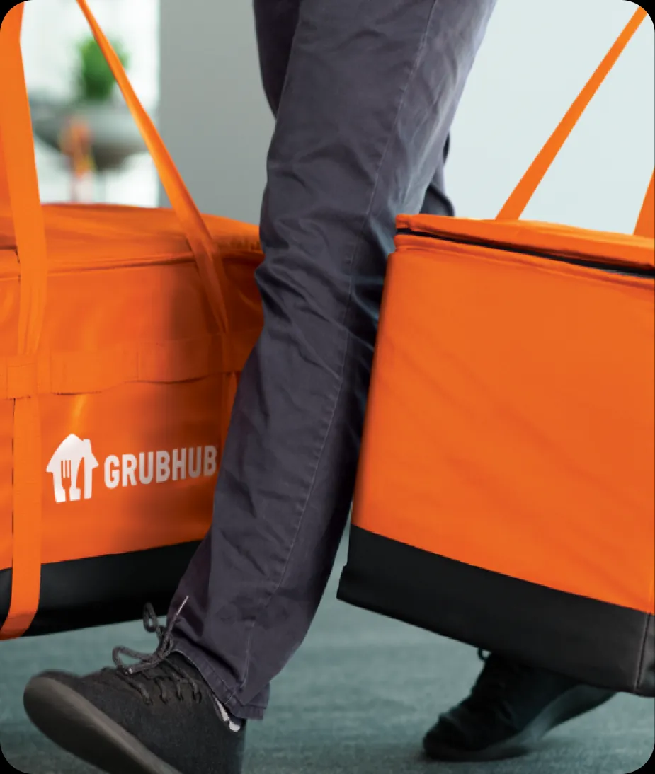 A Grubhub courier carrying two orange insulated delivery bags