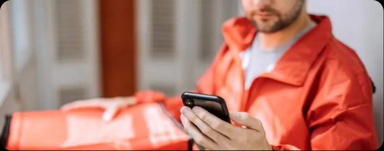 A courier in a red jacket checking an order on his phone