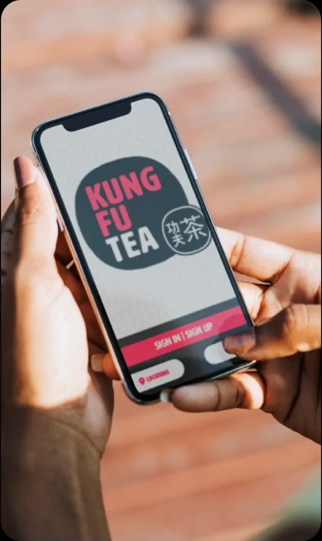 Hands holding a phone showing a Kung Fu Tea ordering app