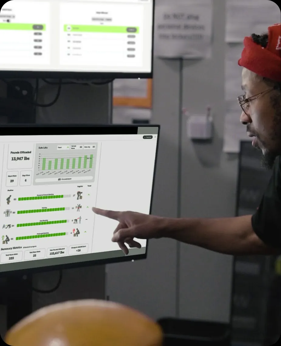 A warehouse worker pointing at a SafeLift dashboard on a screen