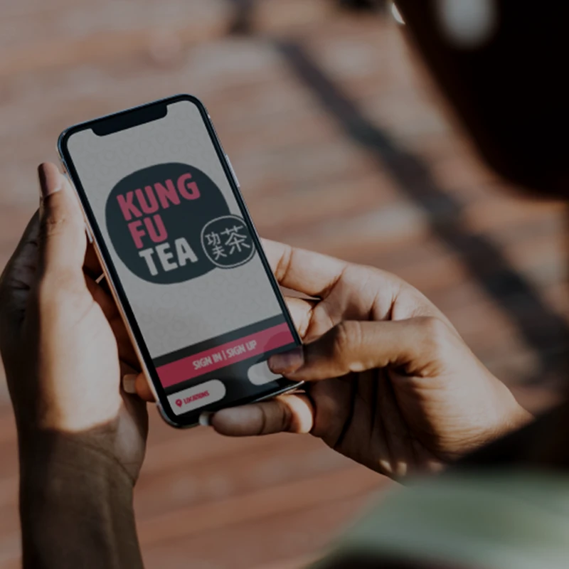 Hands holding a phone showing a Kung Fu Tea ordering app